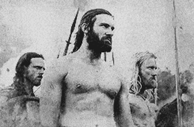 three men are standing next to each other in a black and white photo . one of the men has a beard .