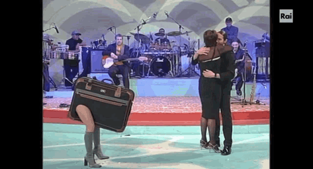 a man and a woman are hugging in front of a band with rai written on the bottom