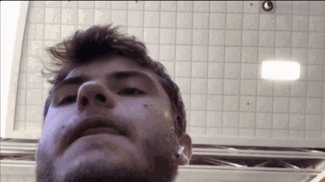 a close up of a man 's face with a white tile wall in the background