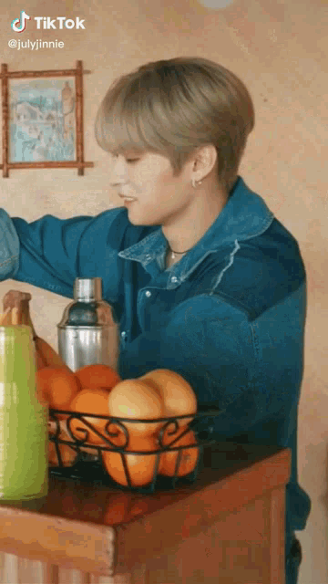 a man in a blue denim jacket is standing next to a basket of oranges