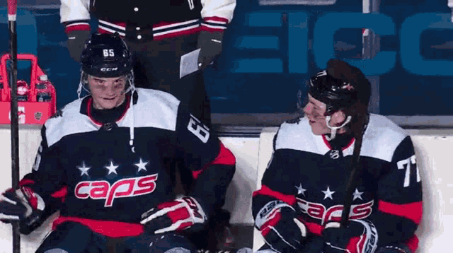 two hockey players wearing caps jerseys are sitting on the ice