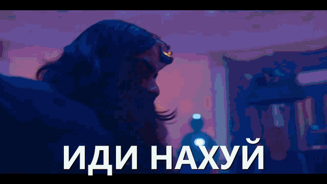 a man with a beard is standing in a dark room with the words " иди нахуй " on the bottom right