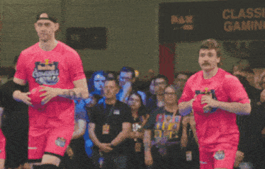 a man in a pink shirt with a crown on it walks with another man