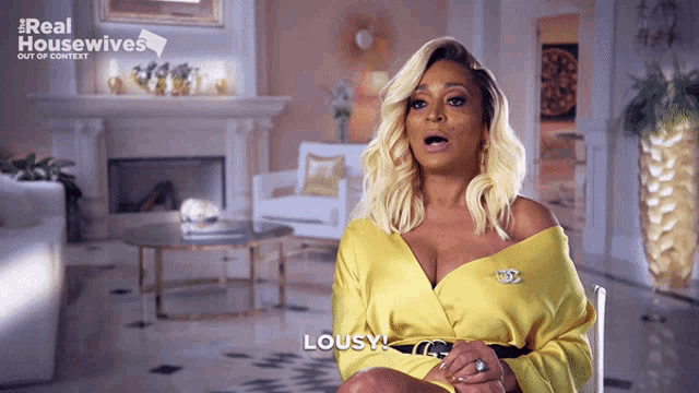 a woman in a yellow dress is sitting in front of a fireplace and says lousy