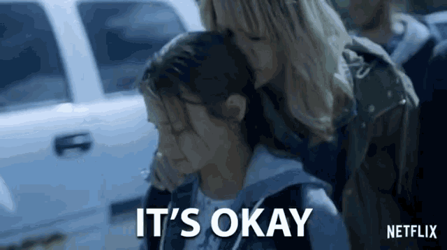 a woman is hugging a little girl and the words it 's okay are written on the screen .