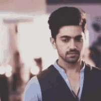 a man with a beard is wearing a vest and a blue shirt .