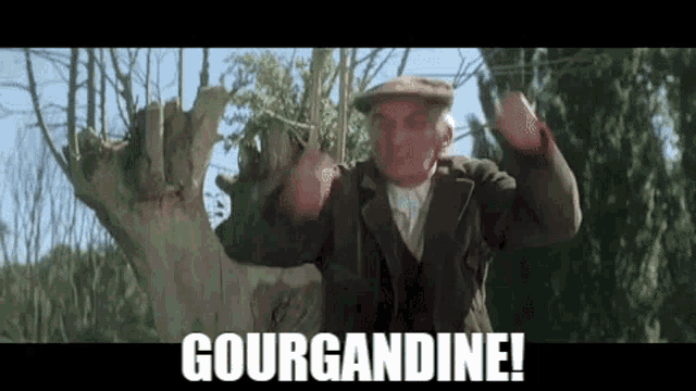 a man in a suit and hat is standing in front of a tree and shouting .