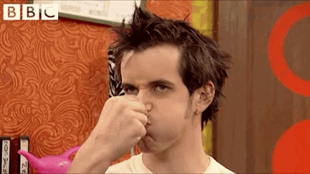 a man holds his nose in front of a bbc sign