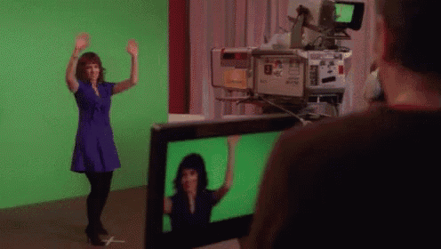 a woman in a blue dress is dancing in front of a green screen while a cameraman looks on .