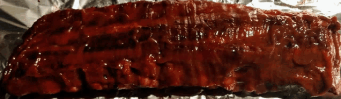 a large piece of meat is covered in sauce on a piece of tin foil