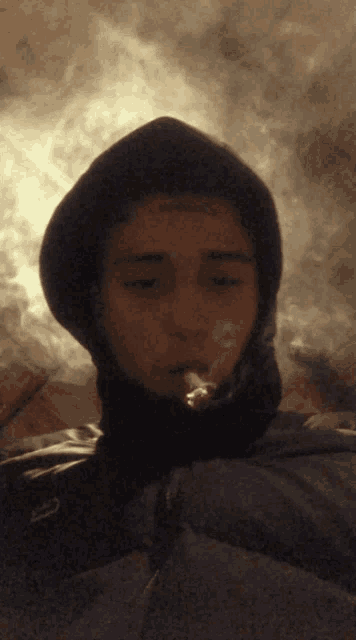 a man in a hooded jacket smoking a cigarette with smoke coming out of his mouth