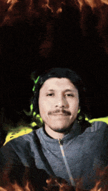 a man with a mustache takes a selfie in front of a fire