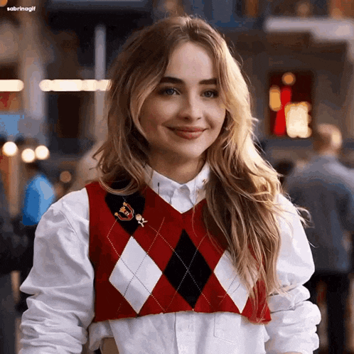 a woman wearing a red and white argyle vest and a white shirt smiles for the camera