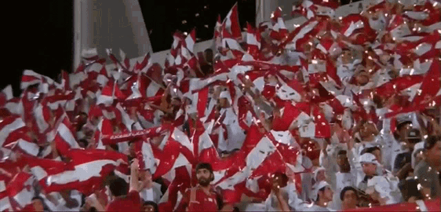 a crowd of people waving red and white flags with the letter l on the front