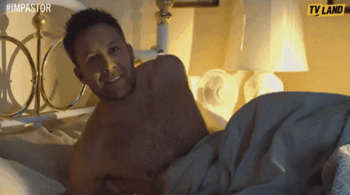 a shirtless man is laying on a bed with a tv land logo in the background