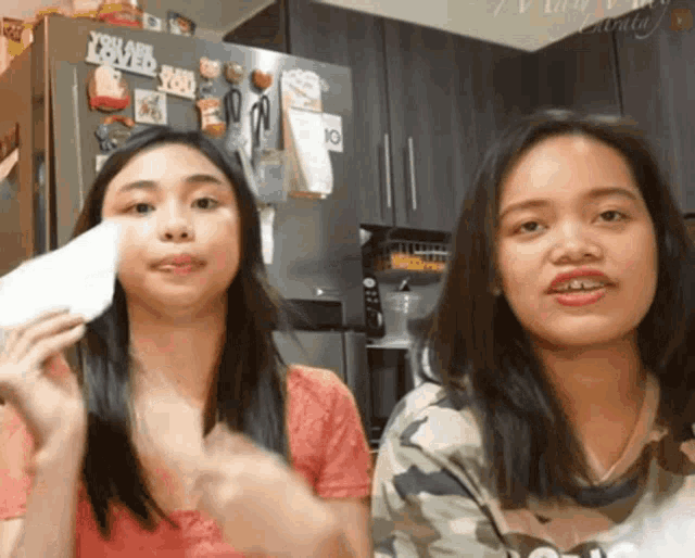 two girls are standing next to each other in front of a refrigerator with a sticker that says yeah i 'm loved