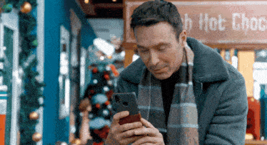 a man is looking at his phone in front of a hot chocolate stand