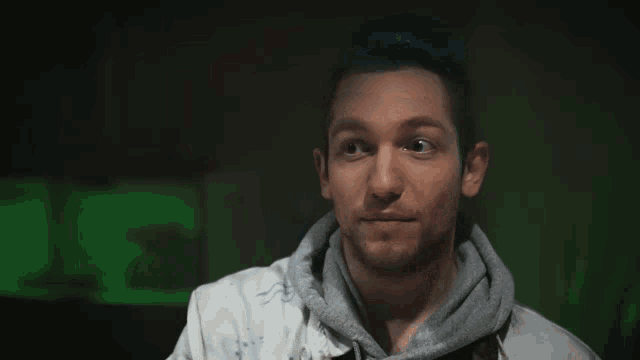 a man with blue hair holds his hand to his chin and looks at the camera