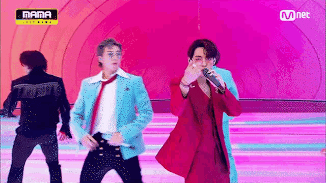 a man in a red suit is singing into a microphone while a man in a blue jacket stands behind him