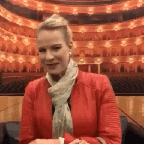 a woman in a red jacket and scarf is sitting in front of a large empty auditorium .
