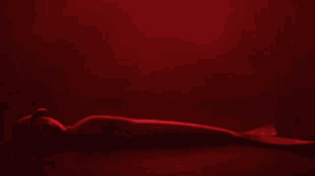 a cartoon character is laying down in a dark room and looking at the camera in a red light .