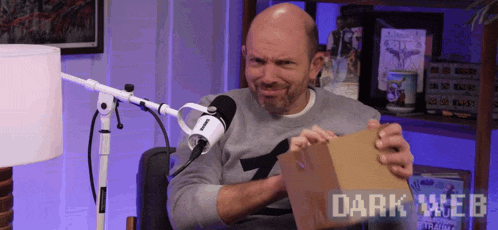 a man is holding a cardboard box in front of a microphone with the words dark web on the bottom right