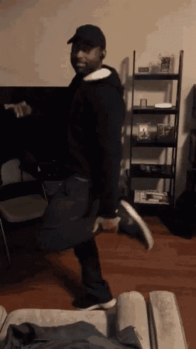 a man is dancing in a living room with a shelf in the background