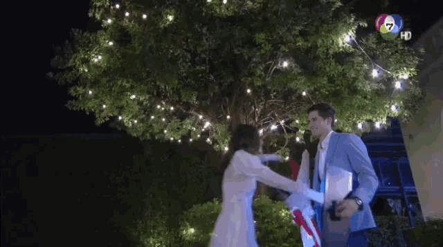 a man and a woman are dancing in front of a tree with lights and the number 7 on the bottom right