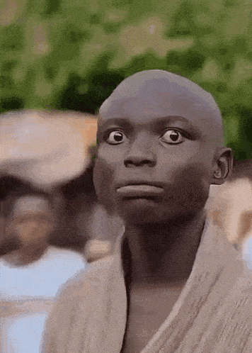 a young man with a bald head is making a funny face while standing in front of a group of people .