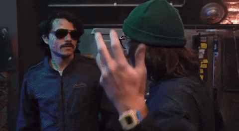 a man wearing sunglasses and a green beanie is talking to another man