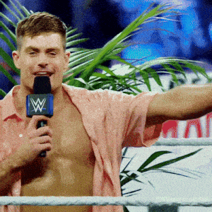 a man in a pink shirt is speaking into a microphone with a w on it