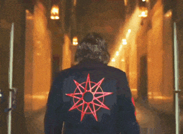 a man in a black jacket with a red star on the back is walking down a hallway