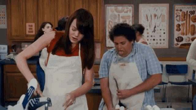 a man and a woman in aprons are standing in a kitchen