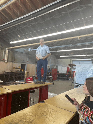 a man in a plaid shirt stands on a table while a girl looks on