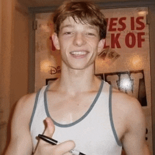 a man in a tank top is smiling in front of a sign that says yes is lk of