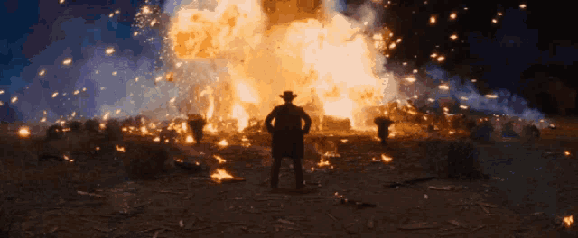 a man in a cowboy hat is standing in front of an explosion