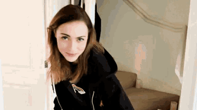 a young woman in a black hoodie is standing in a doorway looking at the camera .