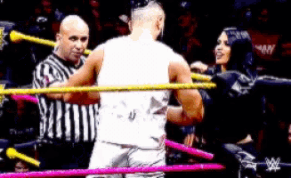 a man in a white shirt is standing in a wrestling ring with a referee