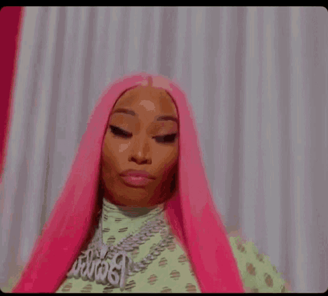 a close up of a woman with pink hair wearing a green shirt and a necklace .