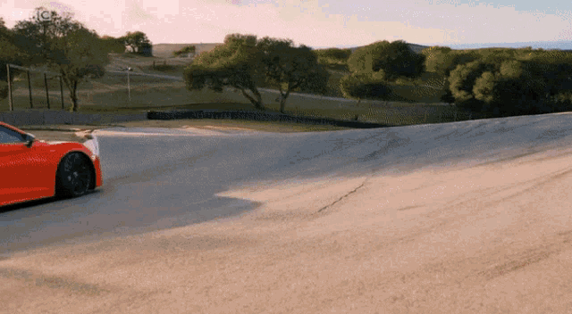 an orange sports car is driving down a dirt road with a sign that says jc on it