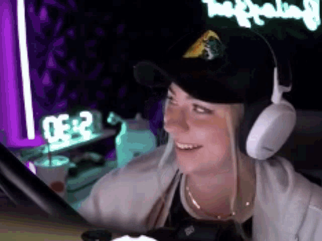 a woman wearing headphones and a hat is looking at a computer screen .