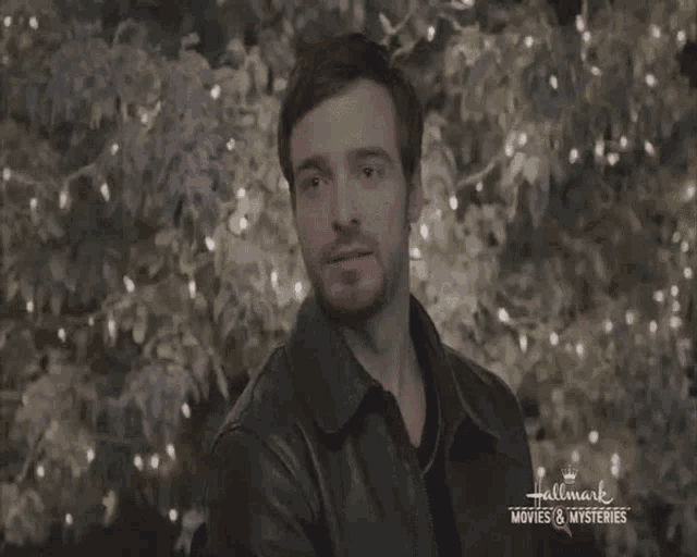 a man is standing in front of a hallmark movie and a tree