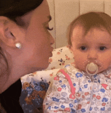 a woman kissing a baby with a pacifier in its mouth