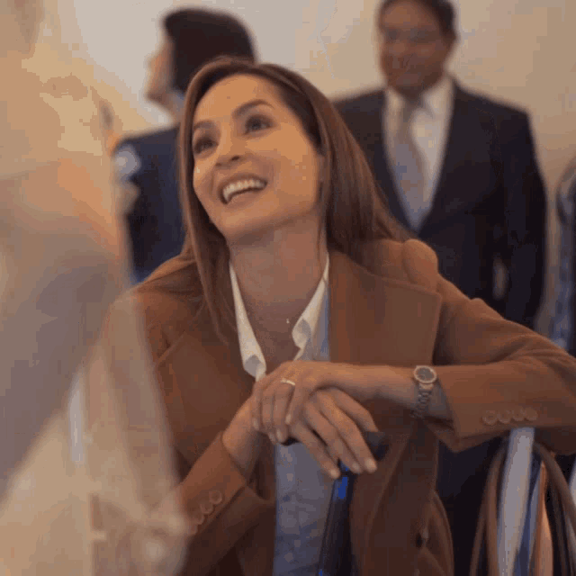 a woman in a brown jacket with a watch on her wrist smiles
