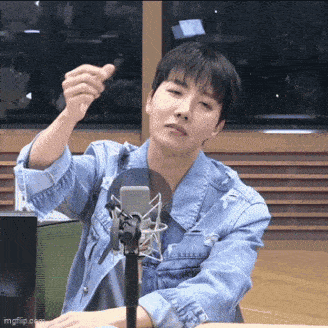 a man in a denim jacket is sitting in front of a microphone and giving a thumbs up