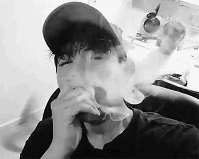 a black and white photo of a man smoking a cigarette in a kitchen .