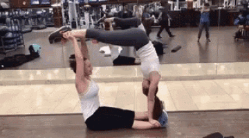 two women are doing a yoga pose in a gym .
