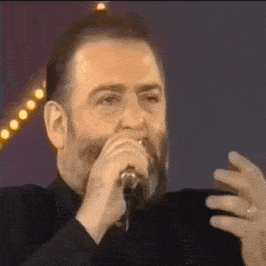 a man with a beard is singing into a microphone and making a face .