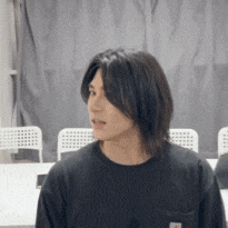 a man with long hair is wearing a black shirt with a pocket on the front .