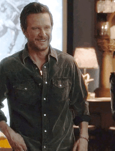 a man in a denim shirt stands in front of a lamp and smiling